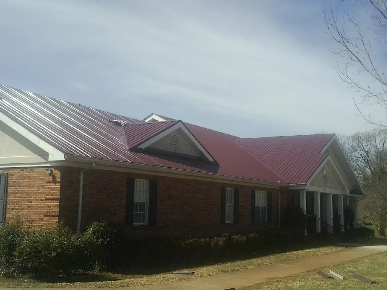 Red metal roof with gabled entries on a long brick building, from a Hail Damage Roof Repair job in Grand Blanc