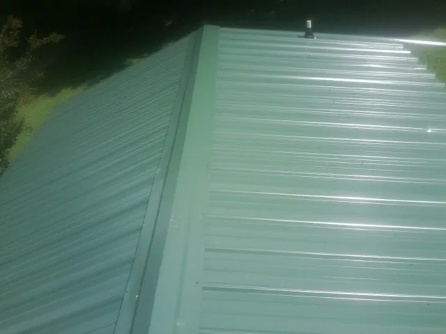 New green metal panels meeting at the ridge of a roof — Flat Roof Repair work by our crew in Grand Blanc