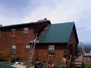 Green metal roof going on a two story log home with ladders set in Grand Blanc