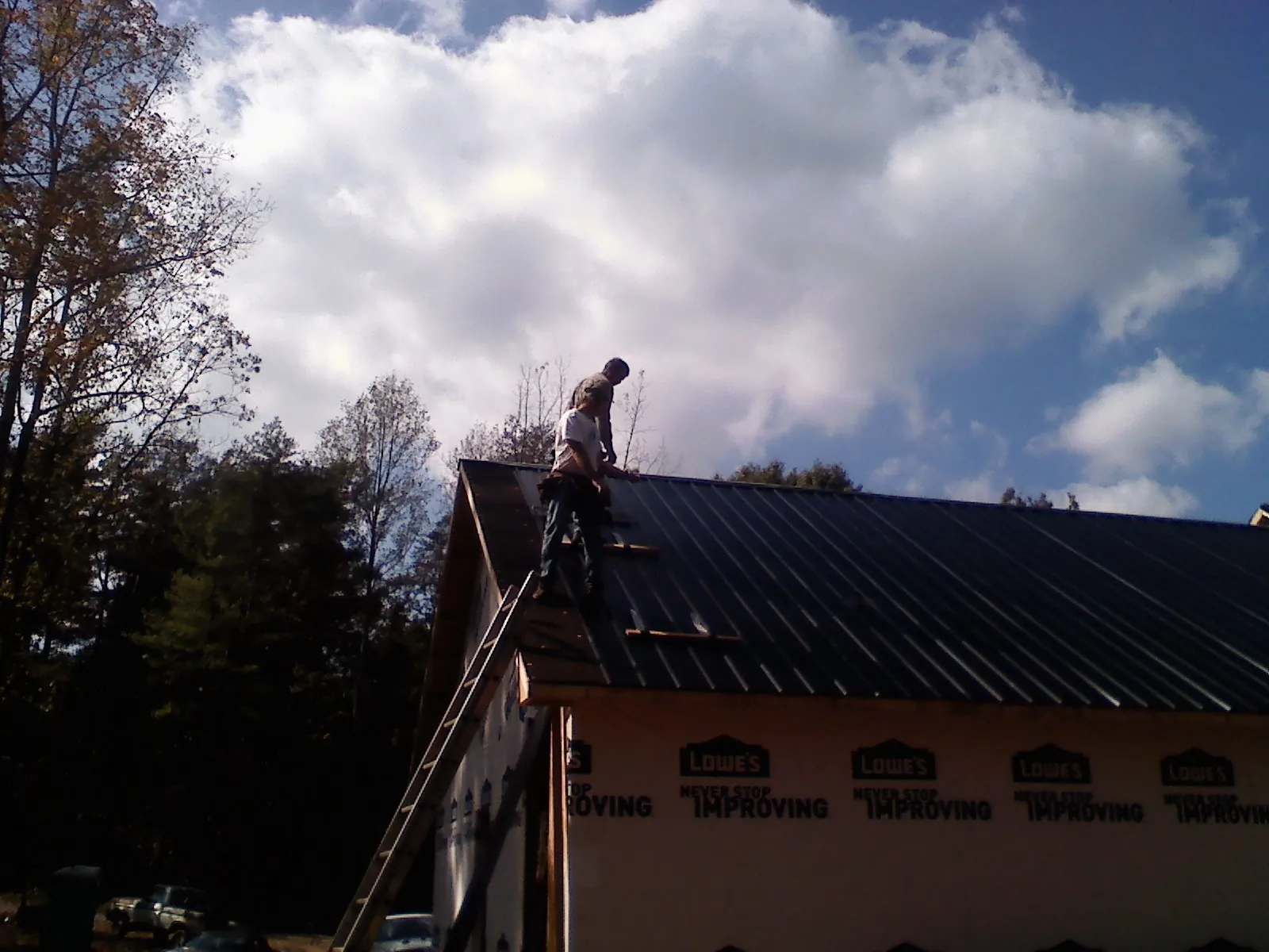 Roofer fastening dark metal panels high against a cloudy sky, from a Roof Inspection job in Grand Blanc