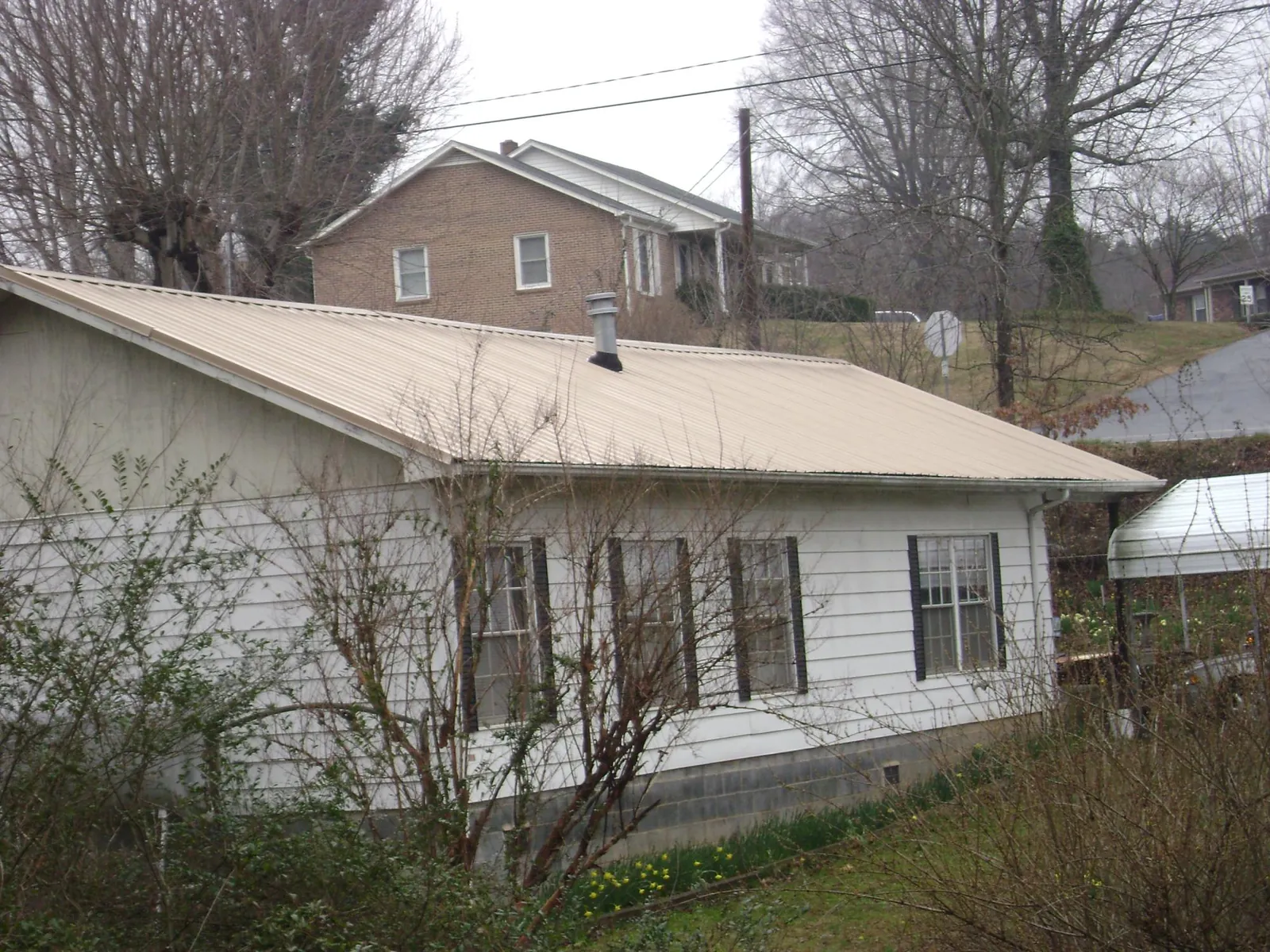 Tan metal roof on a white sided house set into a hillside — Commercial Roofing by Roofing Brothers in Grand Blanc