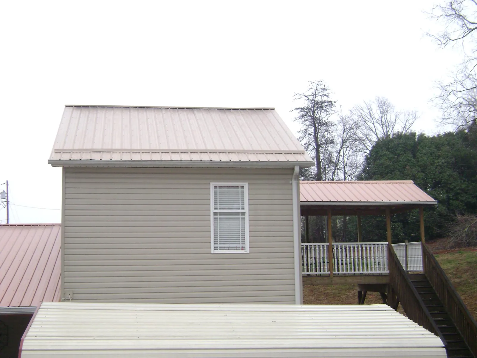 Tan metal roofs on a two story addition and attached porch, from a Roof Replacement job in Grand Blanc